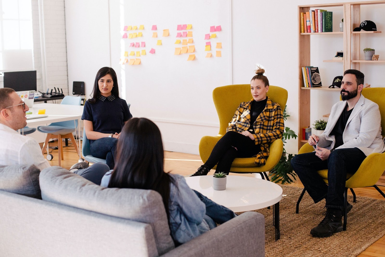 A group of five employees sit around a small round table in discussion.