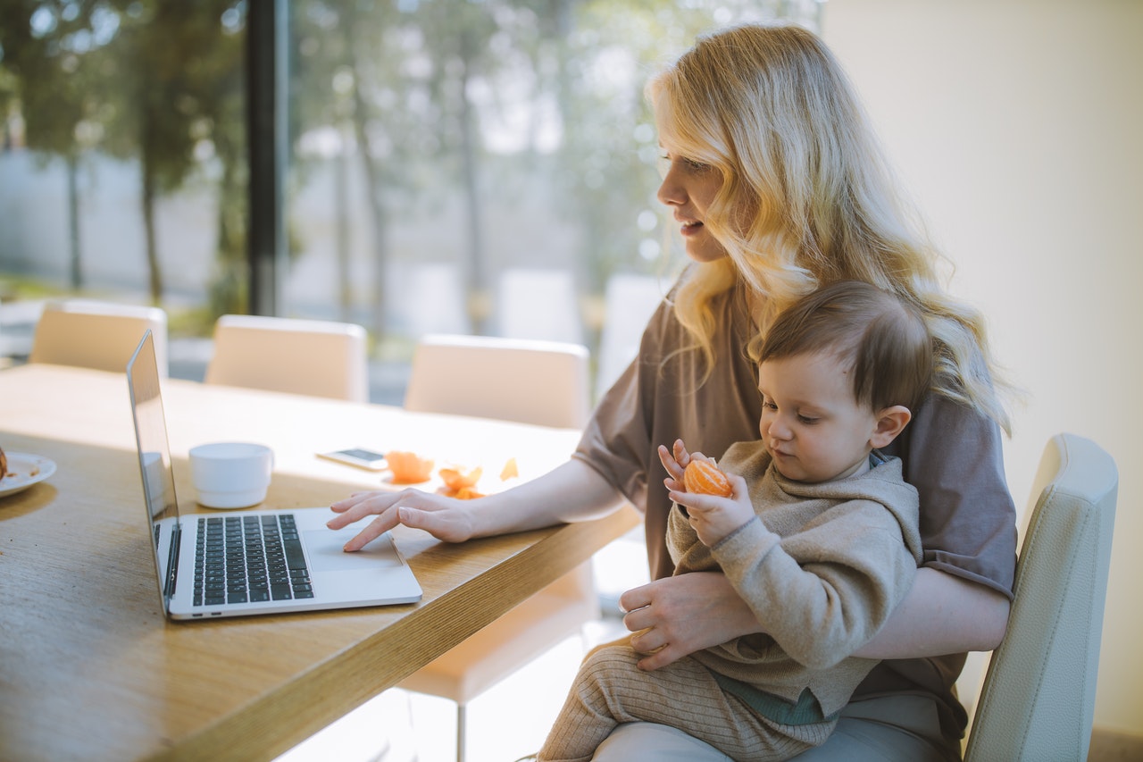 Photo of a remote employee sitting at a table doing work with her son on her lap