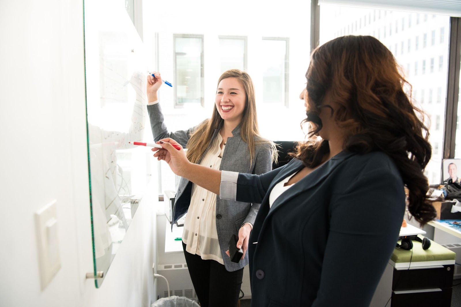 Photo of two employees strategizing and writing on a marker board