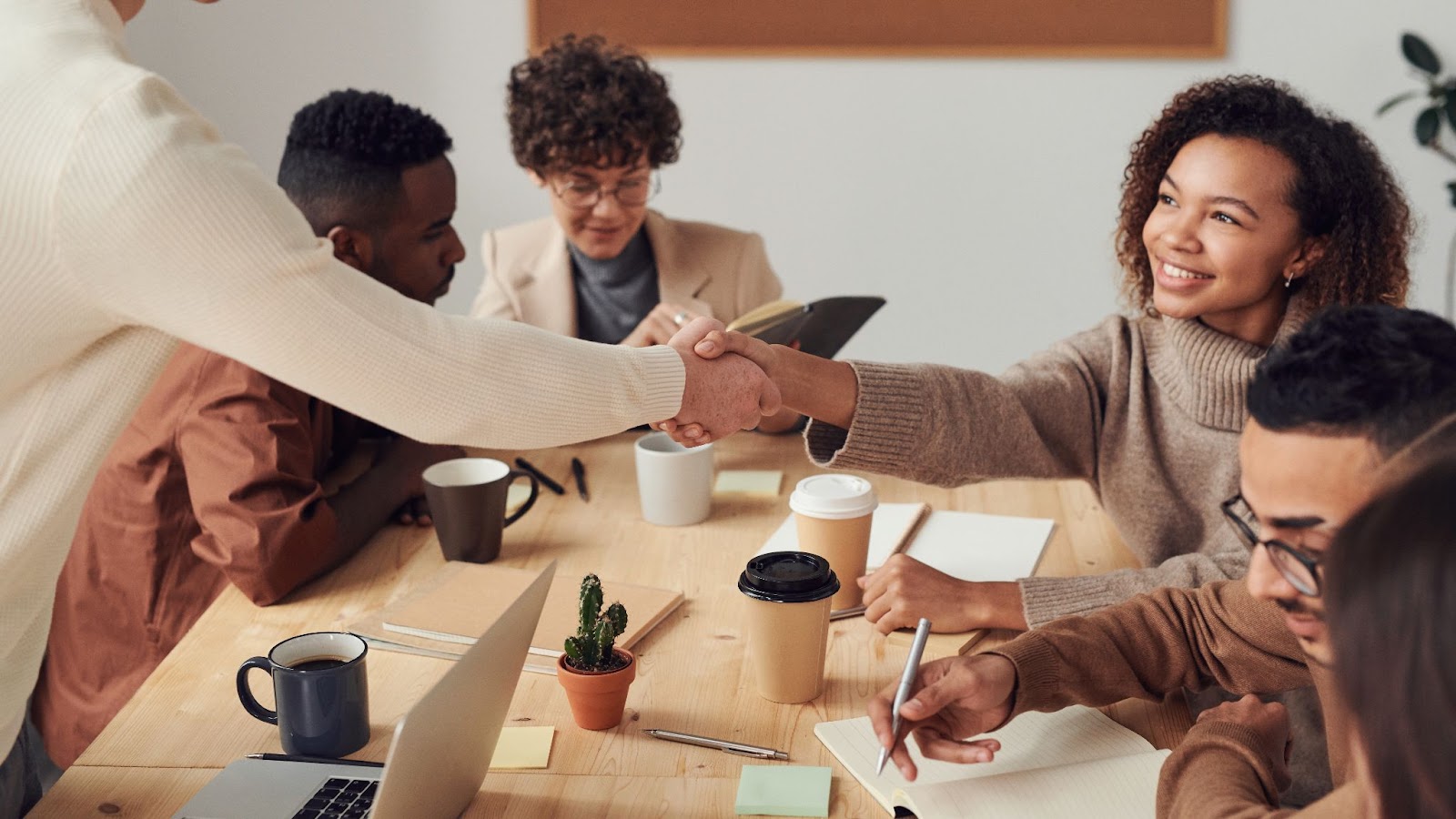 Photo of two employees shaking hands while three other team members work