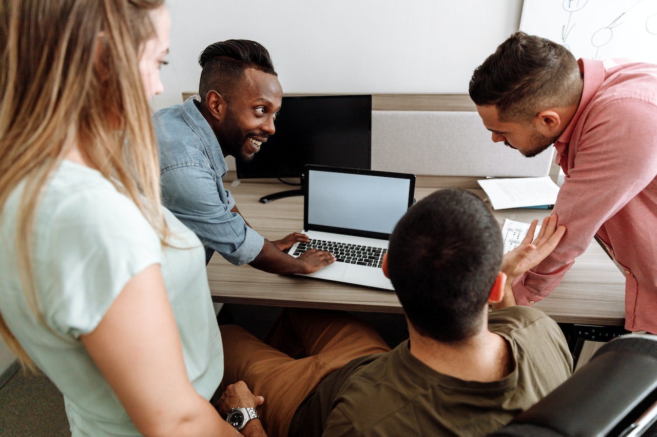 A photo of four employees working together in front of a desk with a laptop.