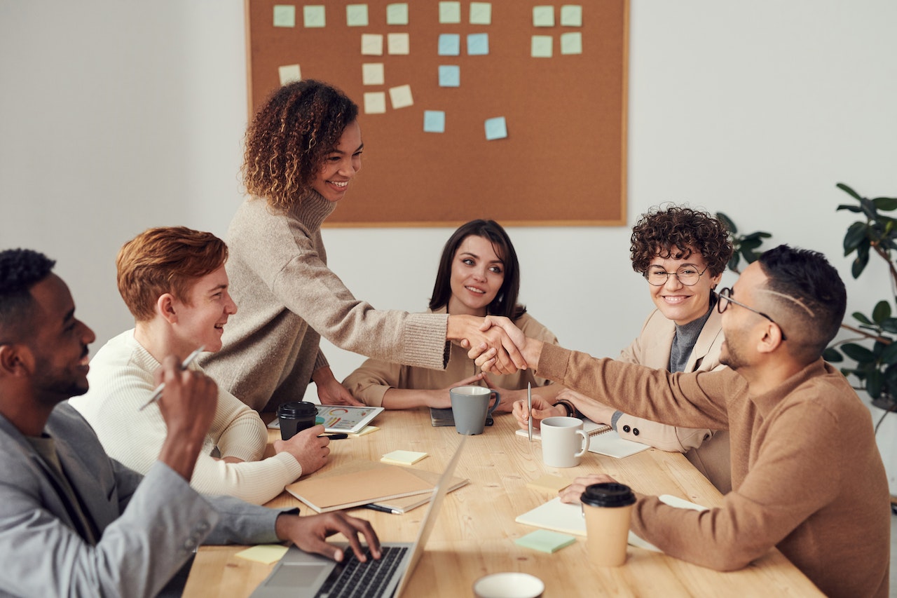 A photo of a group of employees at a meeting table, two of whom are shaking hands.