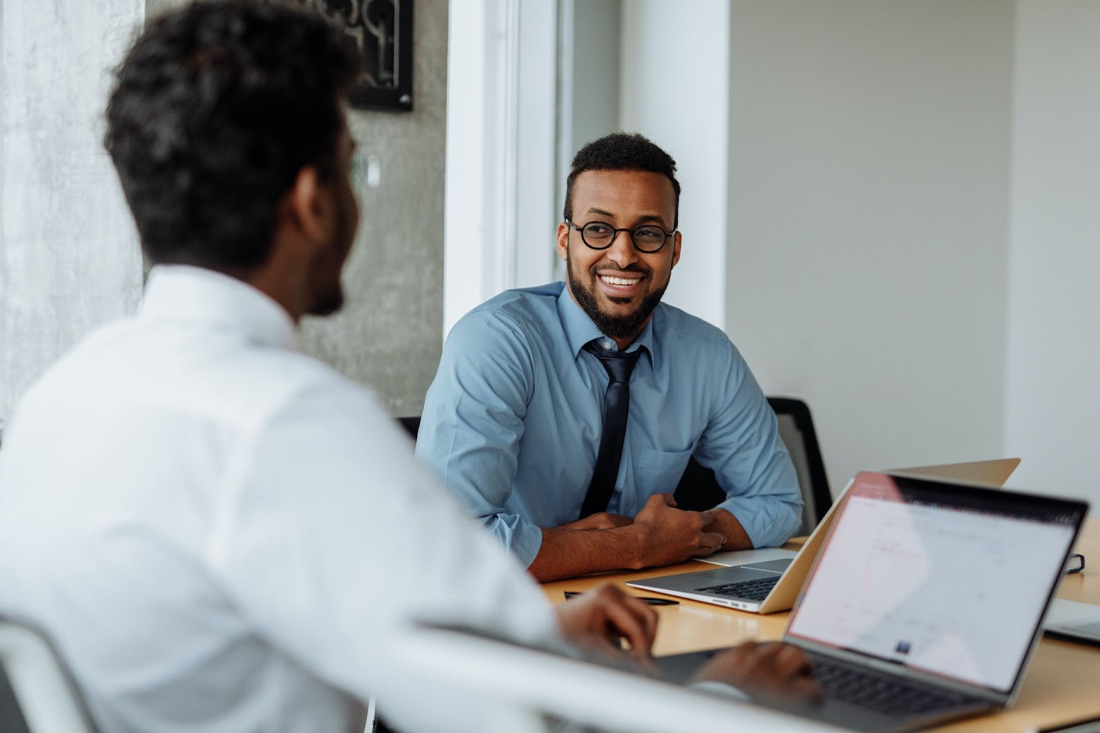 A photo of two employees with laptops sitting together at a table.