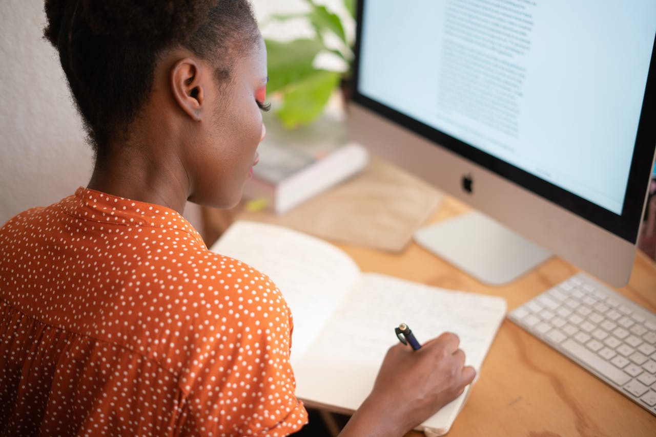 A photo of a professional writing in a notebook at a workplace desk.