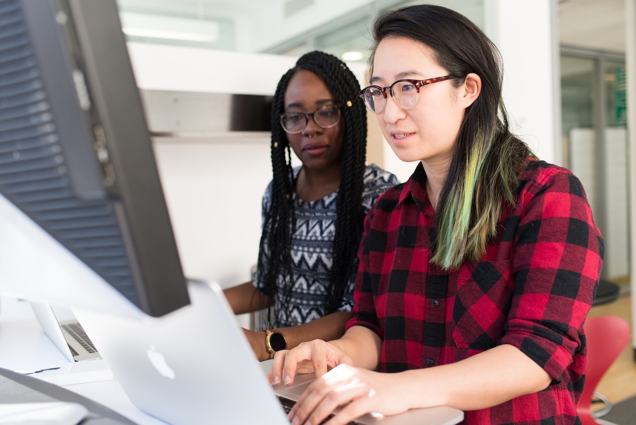 A photo of two employees working in front of a desktop computer.