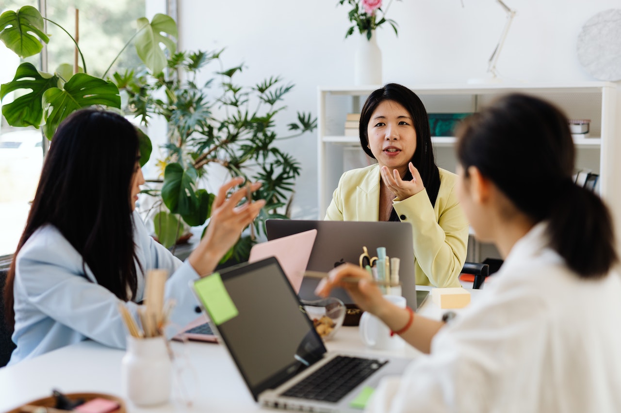 A photo of three colleagues talking and collaborating in a brightly lit workspace.