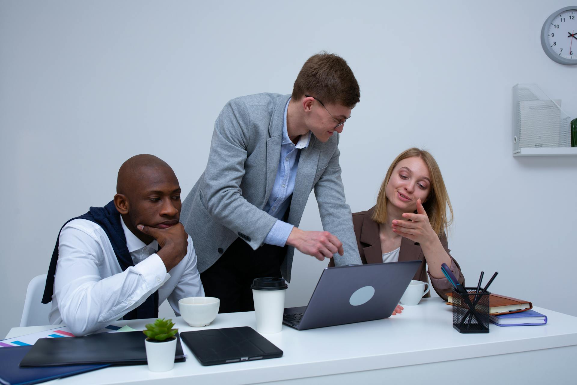 Photo of three employees gathered in front of a desk looking at one laptop.