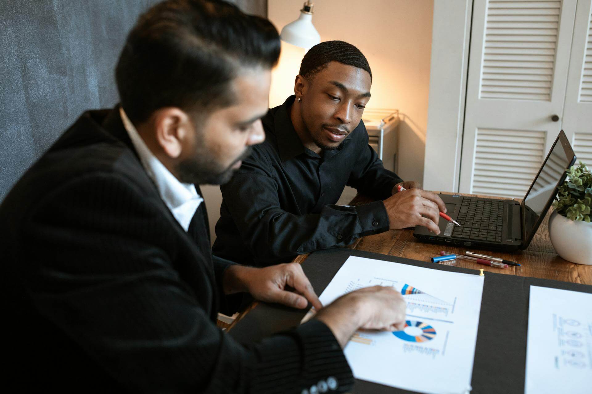 Photo of two employees sitting at a desk with a laptop and charts.