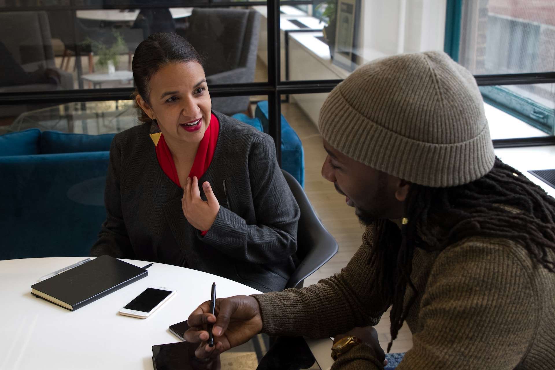 A photo of two professionals sitting at a round table in a meeting room talking.