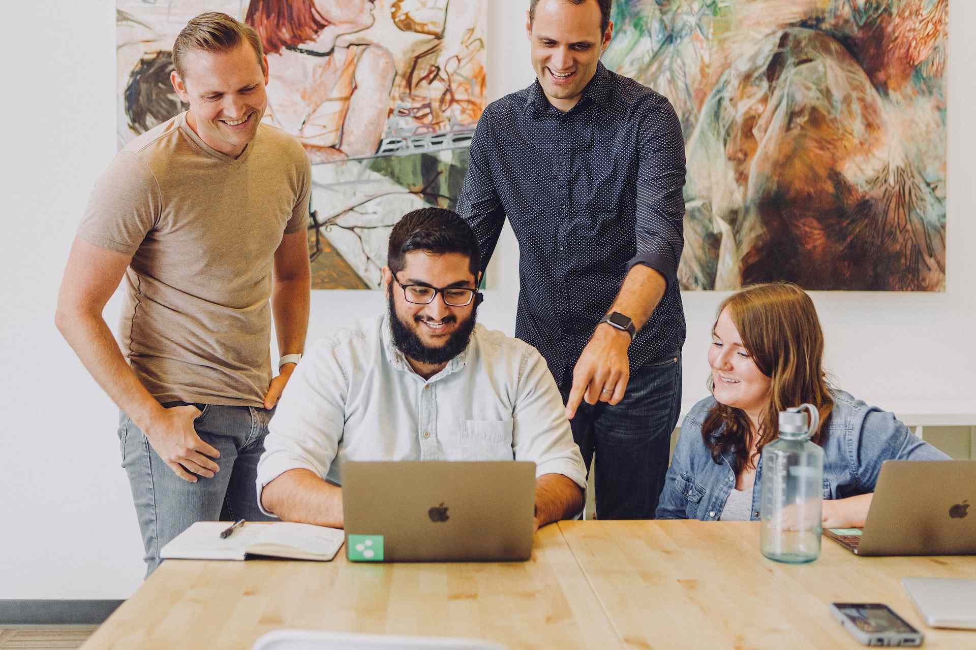 A photo of employees standing in front of a table, looking at a computer.