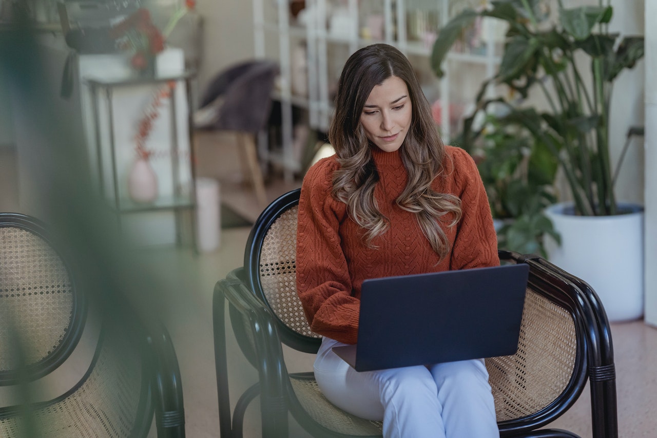 A photo of a remote worker sitting in a chair typing on their laptop.