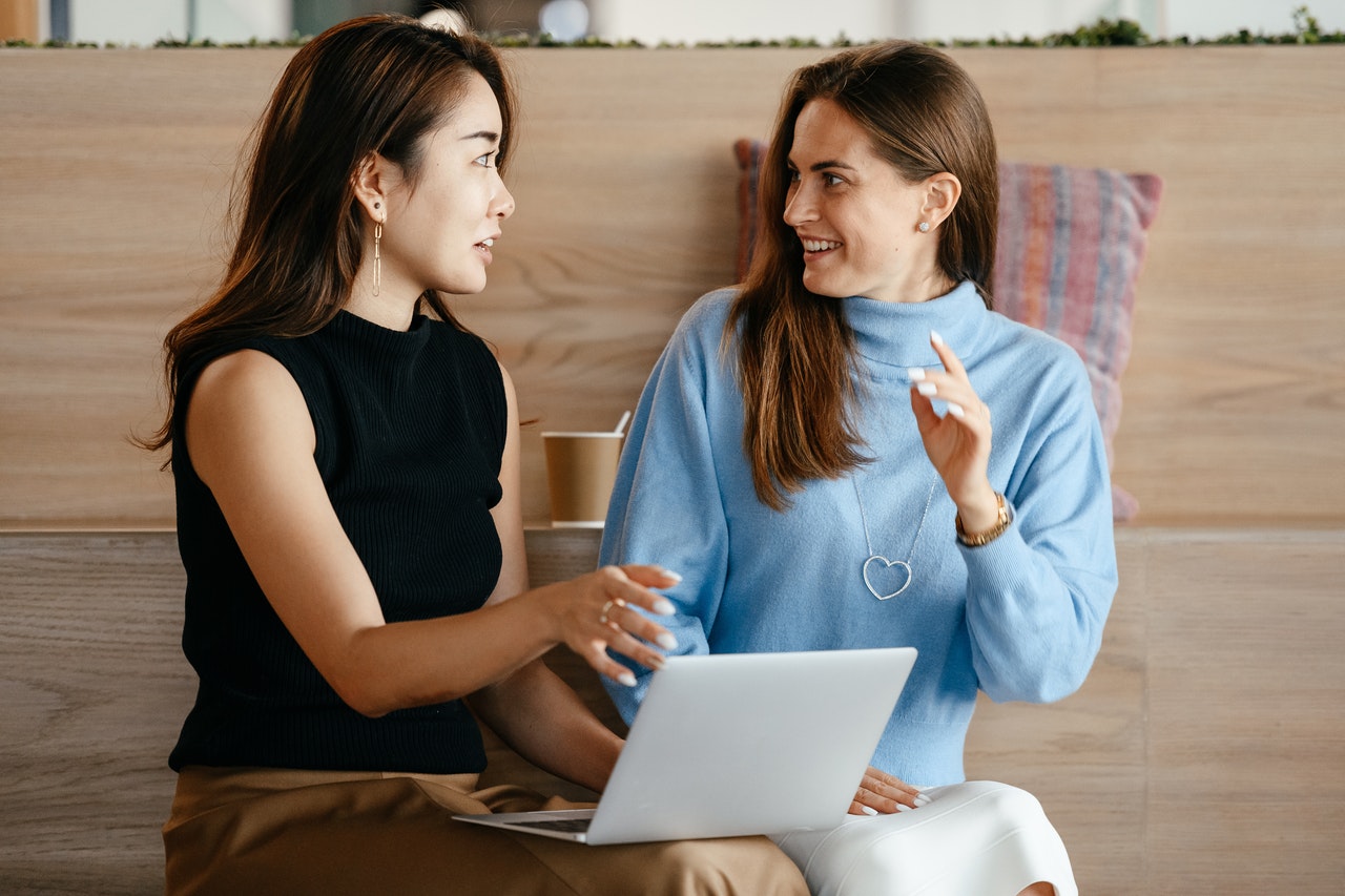 Photo of two women having a conversation while one of them holds an open laptop